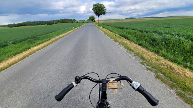Das Lenkrad eines Fahrrads, eine Landstraße und Felder an den Seiten 
