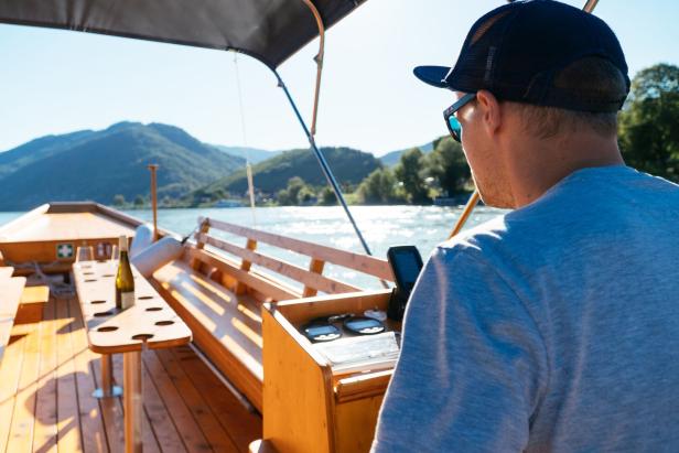 Zillenfahrer am Steuer - vor ihm ein Tisch, worauf Wein steht.