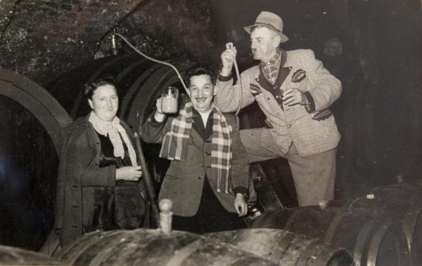 Fröhliche Kellerpartie: Maria und Josef Jakopé stehen um ein Weinfass auf der Kästenburg, festgehalten auf einer Schwarzweißfotografie.