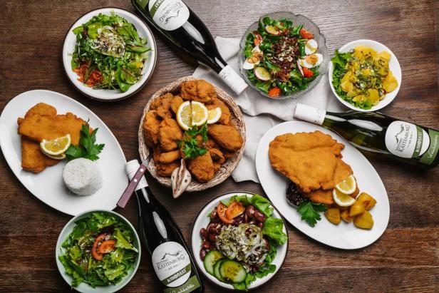 Ein reich gedeckter Tisch mit Steirischem Backhendl, Käferbohnensalat mit Kernöl und Wein.