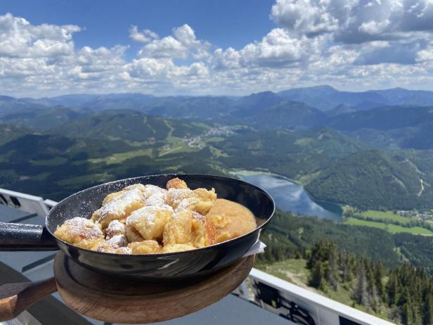 Auf dem Bild ist eine Pfanne mit einem Kaiserschmarrn vor einer schönen Bergkulisse abgebildet.