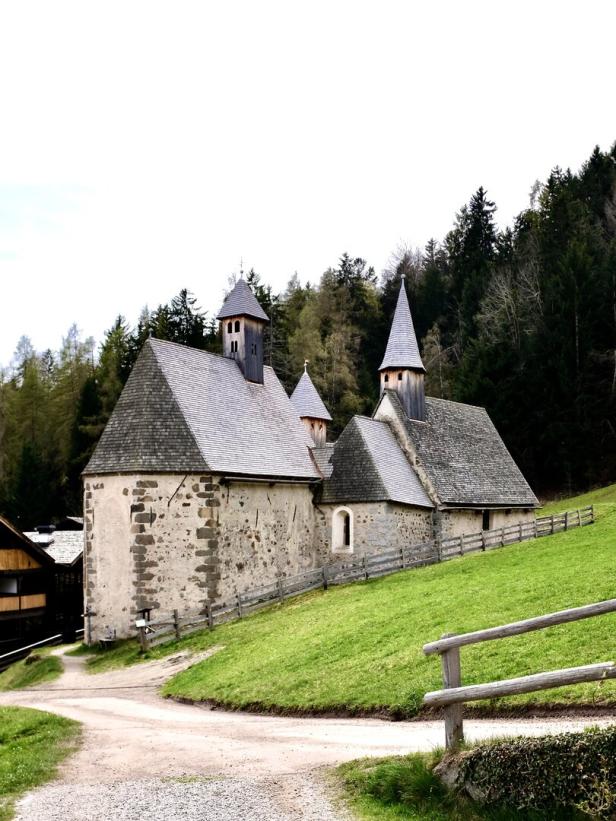 Eine kleine Kirche mit Holzturm steht auf einer grünen Wiese.