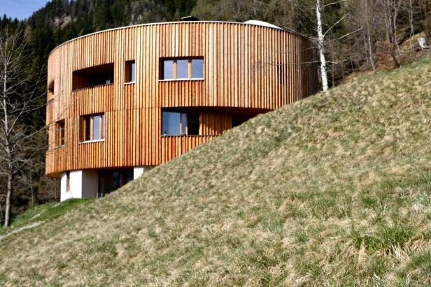 Ein rundes, modernes Holzhaus steht auf einem grasbewachsenen Hügel.