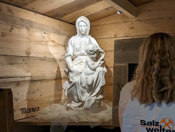 Eine Marmorstatue der Jungfrau Maria mit dem Jesuskind in einer Holzkammer.