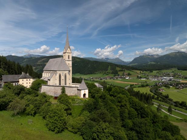 Eine Kirche mit hohem Turm thront über einer grünen Landschaft.