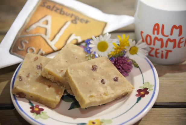 Salzburger Nockerl-Konfekt auf einem Teller mit Blumen und einer Tasse „Alm Sommer Zeit“.