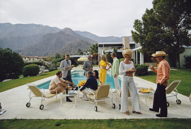 Poolside Social Poolszene: Menschen sethen und sitzen um einen Pool, sie unterhalten sich angeregt. Im Hintergrund: Berge