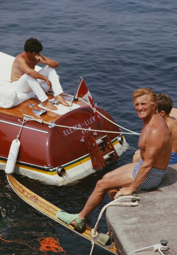 Kirk Douglas In Antibes Kirk Douglas in Badehose sitzt an der Hafenmauer, er hat Wasserksi an, vor ihm ein Motorboot