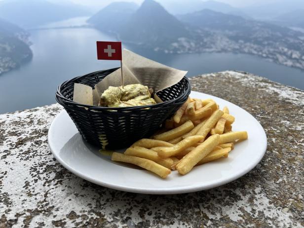 Ein Korb mit Chicken Nuggets mit Schweizer Flagge und Pommes vor einer Bergkulisse.