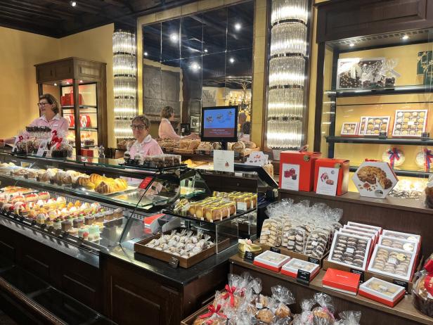 Zwei Verkäuferinnen stehen hinter einer Theke voller Kuchen und Gebäck in einem Feinkostladen.