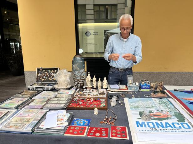 Ein Mann steht an einem Stand mit Sammlerstücken, darunter Banknoten, Münzen und Schmuck.
