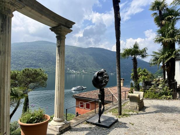 Blick durch eine Säulenstruktur auf den Parco Scherrer in Morcote mit See und Bergen.