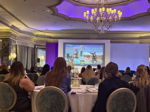 Group of mainly women in a elegant conference room look at the podim, where Sophie Morgan presents a speech in Inclusive Travel.