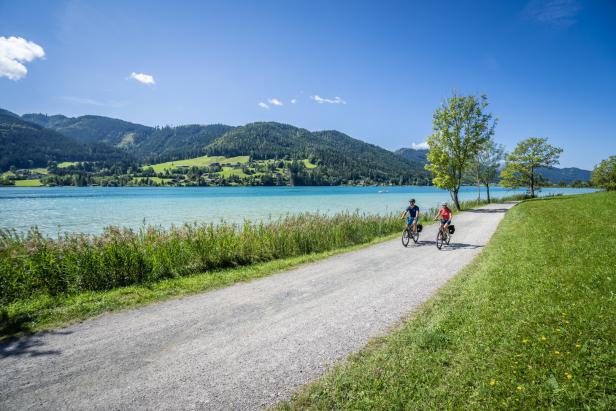 Zwei Personen fahren mit Fahrrädern auf einem Weg entlang eines Sees.