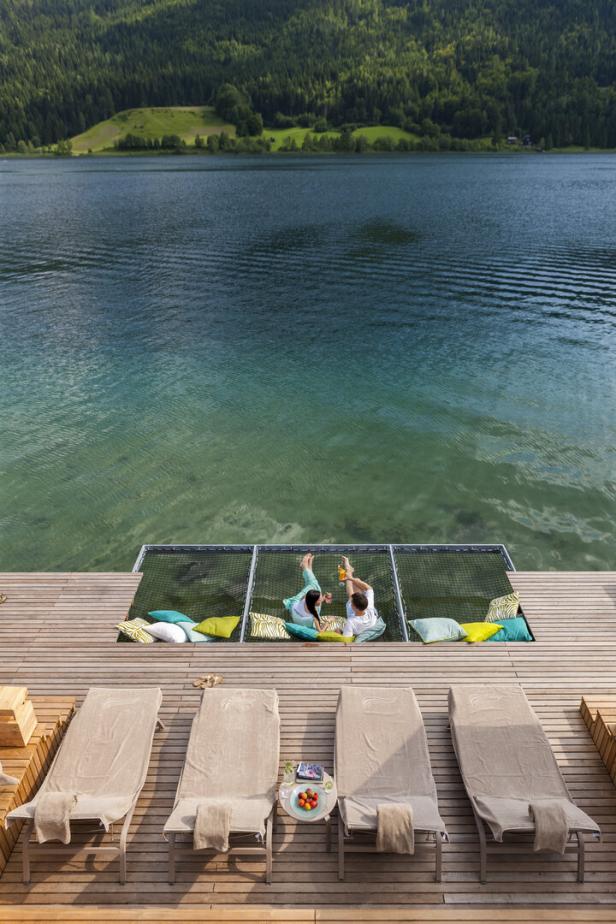 Ein Paar entspannt in einer Hängematte über einem klaren See, umgeben von grünen Hügeln.