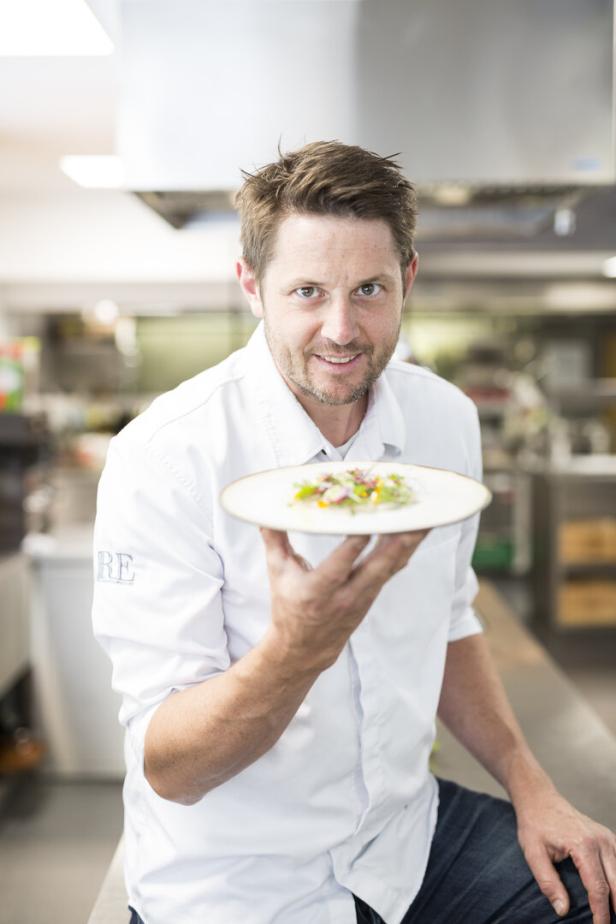 Ein Koch präsentiert ein Gericht in einer Restaurantküche.