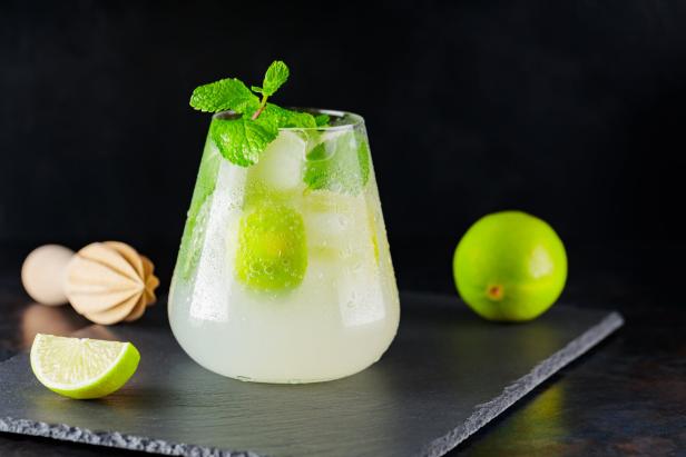 Mojito cocktail, lime and wooden juicer on a dark background. Summer cocktail mojito with lime and mint on a slate board. Summer drink concept