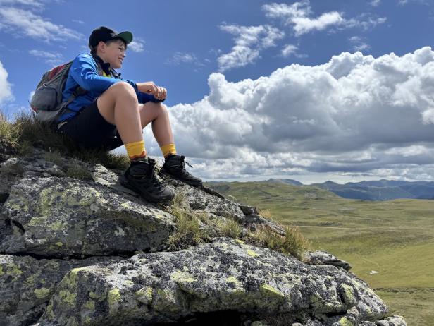 Kind sitzt auf einem Felsen und schaut in die Landschaft