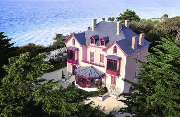 Ein großes, rosafarbenes Haus mit dunklem Dach steht an der Küste.