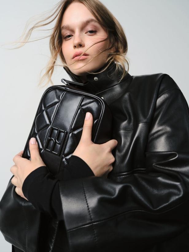Look von Högl Eine Frau mit Lederjacke hält eine schwarze, gesteppte Handtasche.