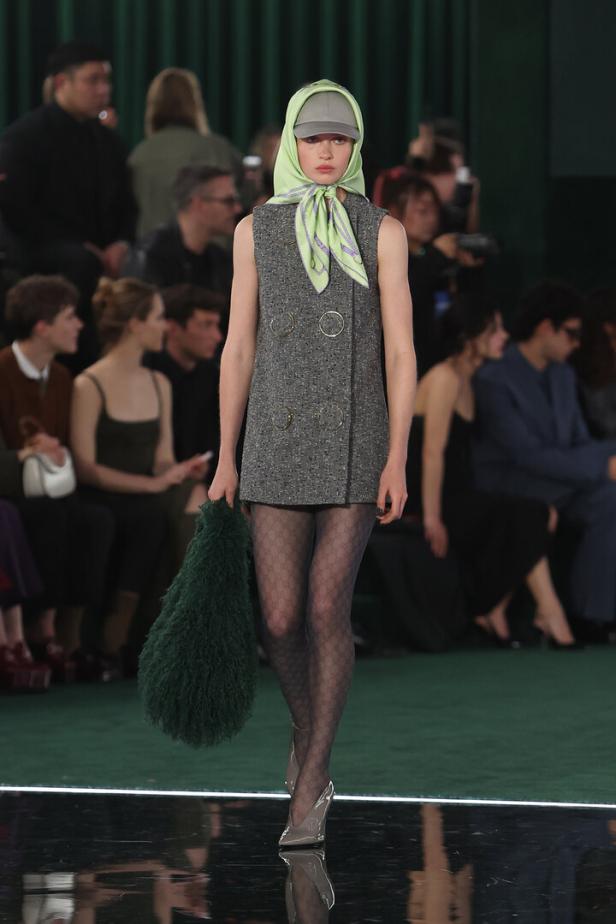 Ein Model mit Kopftuch, Kappe und Tweedkleid auf einem Laufsteg.