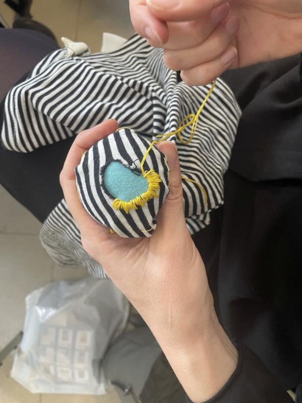 Eine Person näht ein Loch in einem schwarz-weiß gestreiften Stoff mit gelbem Faden.