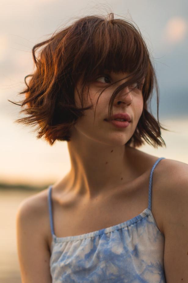 Asian woman in dress on sunset sky background. Bobbed hair. Summer. Mole on skin. Beauty portrait Eine junge Frau im Spaghettiträgerkleid mit Bob-Frisur und dunkelbraunem Haar.