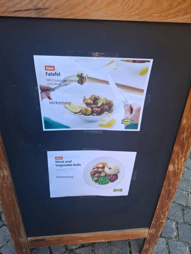 Eine Tafel mit zwei Zettel beklebt, auf denen die neuen Ikea-Speisen gezeigt werden. 