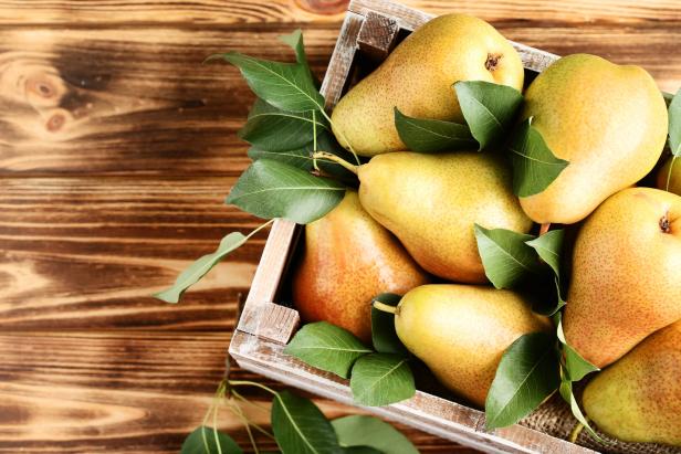 Ripe pears and green leafs in crate on brown wooden table