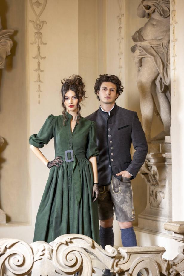 Ein Paar in Trachtenmode posiert vor einem verzierten Hintergrund.