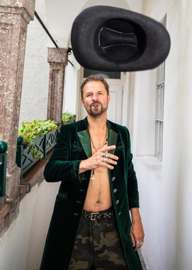 Ein Mann mit Zigarre, offenem grünen Samtfrack und fallendem Hut in einem Durchgang.