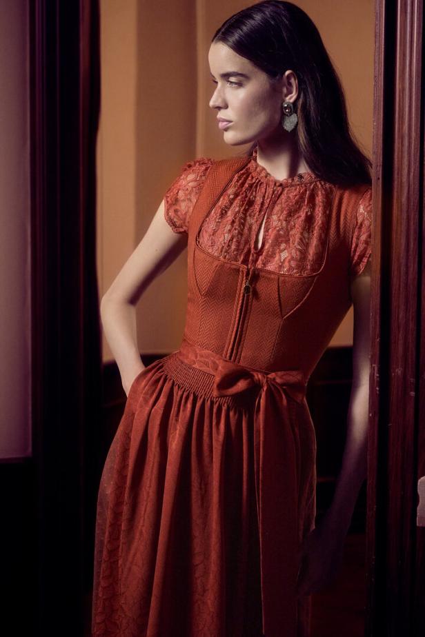 Eine Frau in einem roten Kleid mit Spitzendetails posiert vor einer Tür.