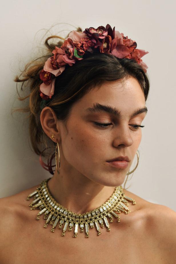 Eine Frau mit Blumenkranz, goldenen Ohrringen und einer Halskette mit Spiegeldetails.