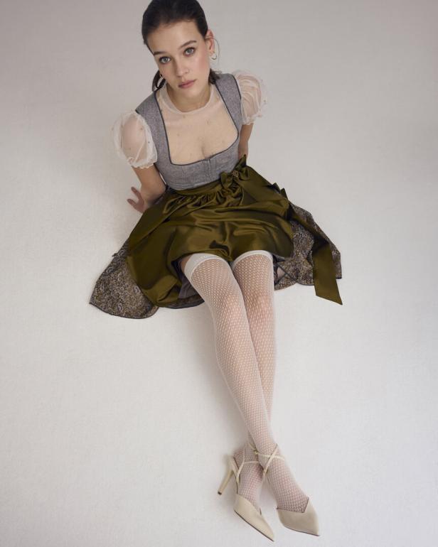 Eine junge Frau sitzt im Dirndl und weißen Kniestrümpfen auf dem Boden.