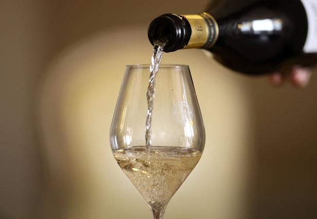 Aus einer Flasche wird Champagner in ein Glas eingeschenkt.