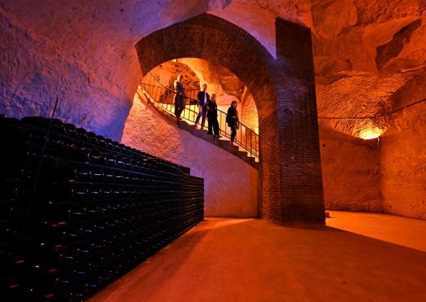 FRANCE-US-EU-ECONOMY-TRADE-TARIFFS-ALCOHOL-DIPLOMACY Menschen steigen eine Stufe in einen riesigen Keller hinab. Unten stehen Regale voll mit Champagnerflaschen.
