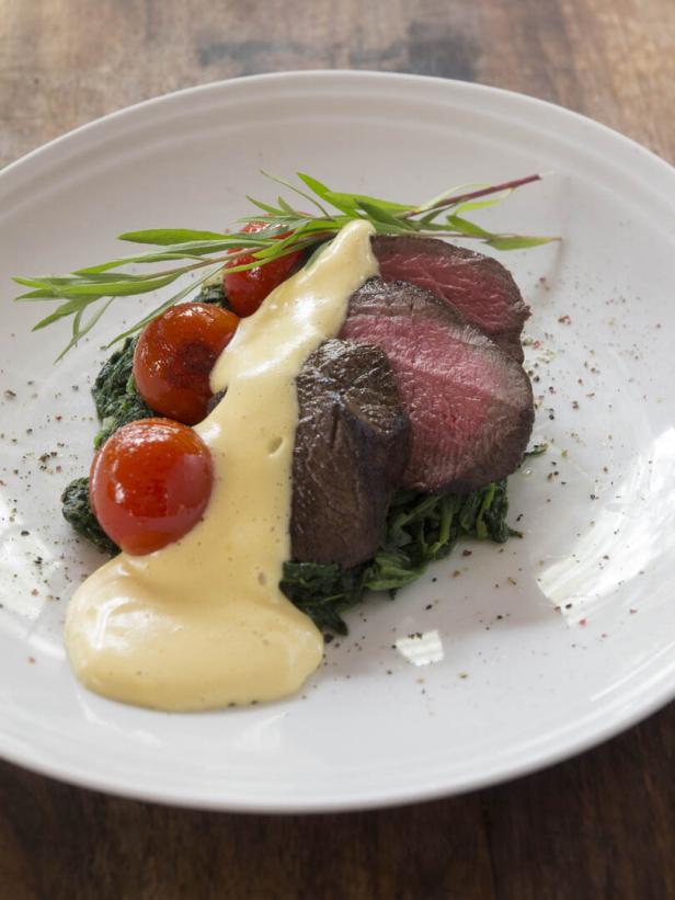 Ein Teller mit Steak, Spinat, Tomaten und Sauce Hollandaise.