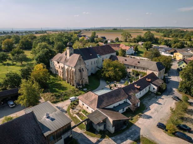 Ein großer Gebäudekomplex am Wagram mit Kapelle und Innenhof, rundherum sind Bäume, Wiesen und Felder.