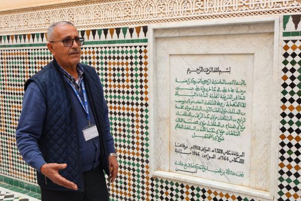 Abdul führt Touristen durch Marokko, hier vor einer Tafel in Meknes.
