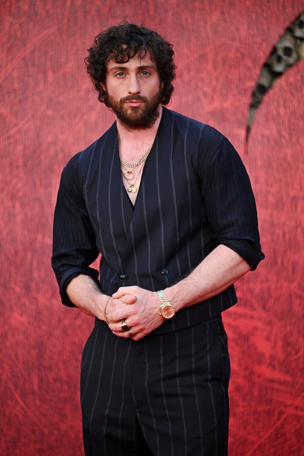 Aaron Taylor-Johnson Aaron Taylor-Johnson posiert vor einem roten Hintergrund.