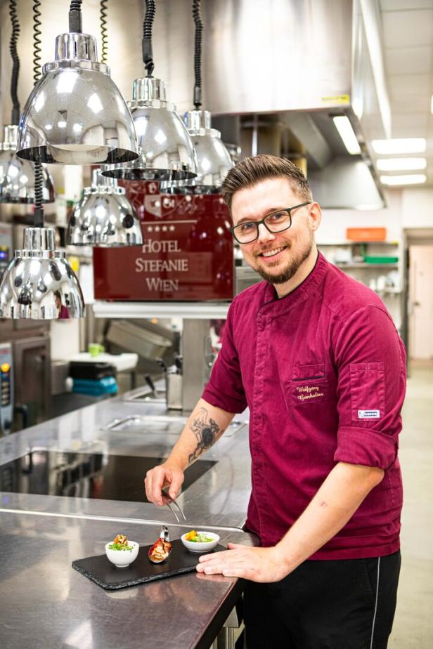 Ein Koch des Hotel Stefanie Wien garniert Speisen in einer Restaurantküche.