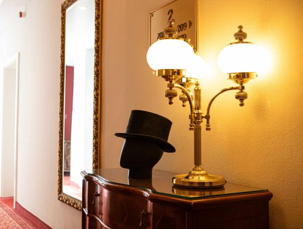 Ein Zylinderhut steht auf einer Kommode neben einer goldenen Lampe.