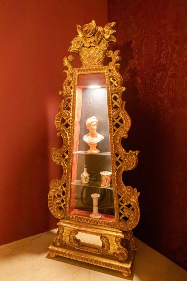 Ein reich verzierter, goldener Schrank mit einer Büste und kleinen Vasen darin.