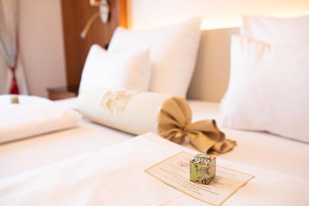 Ein dekoriertes Kissen und eine kleine Schachtel auf einem Hotelbett.