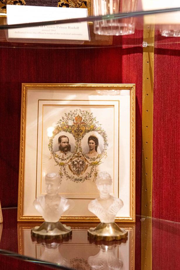 Ein gerahmtes Porträt von Kronprinz Rudolf und seiner Frau, umrahmt von floralen Elementen und zwei Büsten.