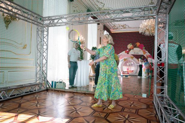 Eine Frau mit Tennisschläger in einer Anlage, bei der man die Kraft des Tennis-Aufschlags testen kann. Mitten in den Prunkräumen der Wiener Hofburg.