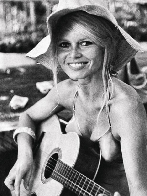 Brigitte Bardot mit Hut und Gitarre lächelt.