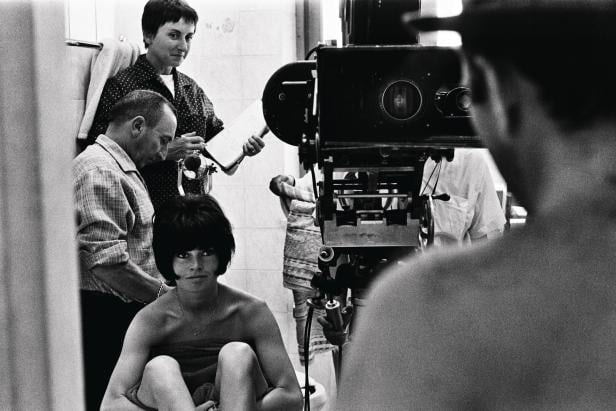 Eine junge Frau, in ein Handtuch gehüllt, vor einer alten Filmkamera am Set.
