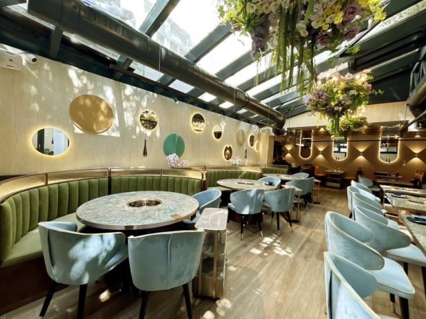 Ein elegant eingerichtetes Restaurant mit runden Tischen und grünen Sitzbänken unter einem Glasdach.