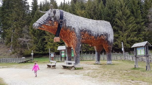 Ein kleines Mädchen geht auf eine große Kuhskulptur aus Holz zu.
